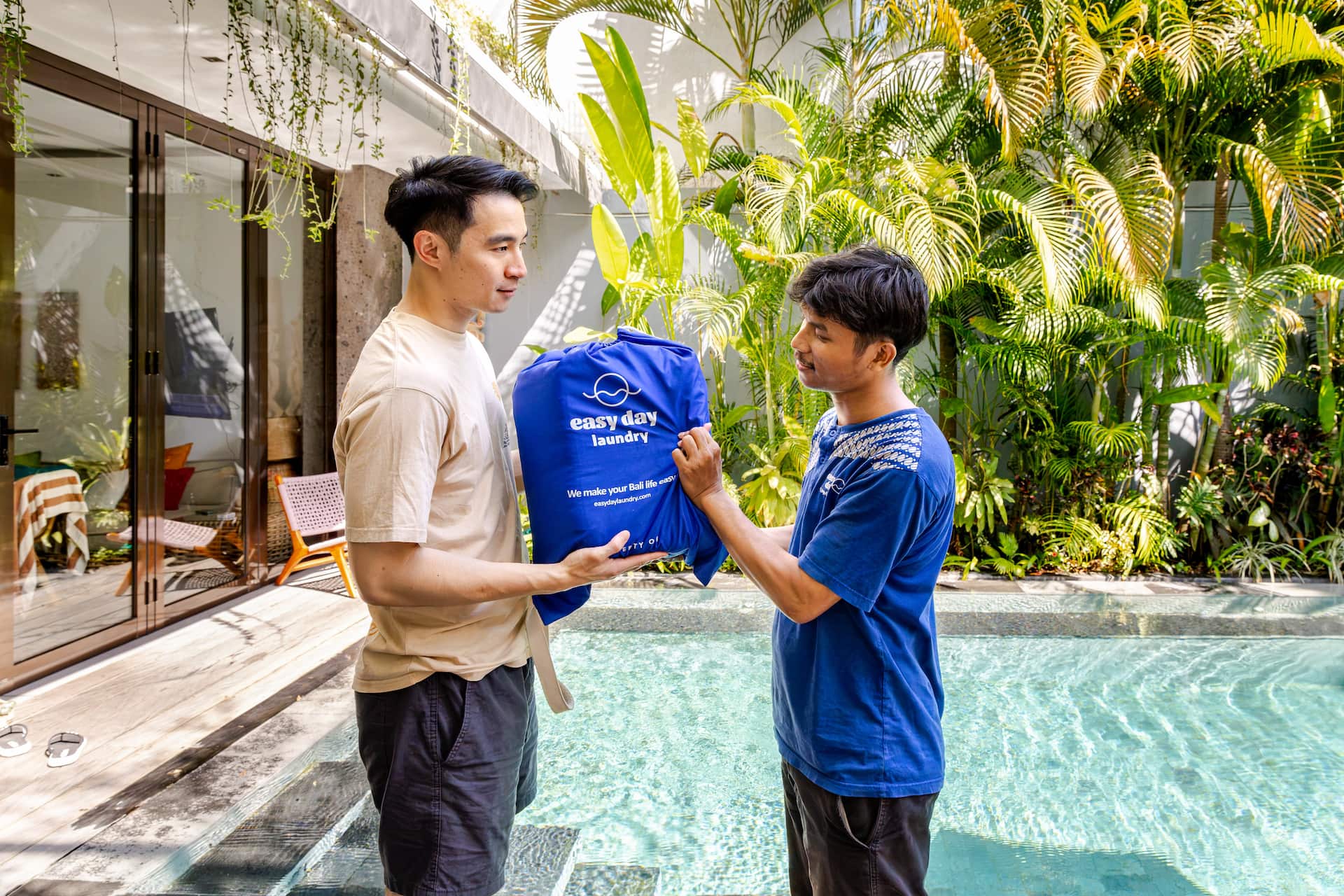 Easy Day Laundry team member handing a branded laundry bag to a customer by a villa pool